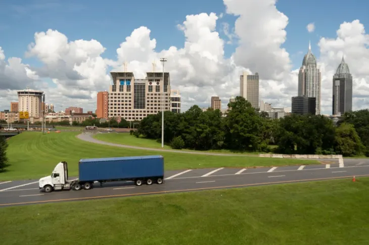 a semi truck on a road with Mobile, Alabama, in the background