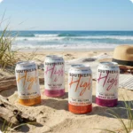 SOUTHERN HIGH | BOOST D9-THCV-YERBA MATE SELTZER | 15MG_LIFESTYLE Four colorful seltzer cans on beach