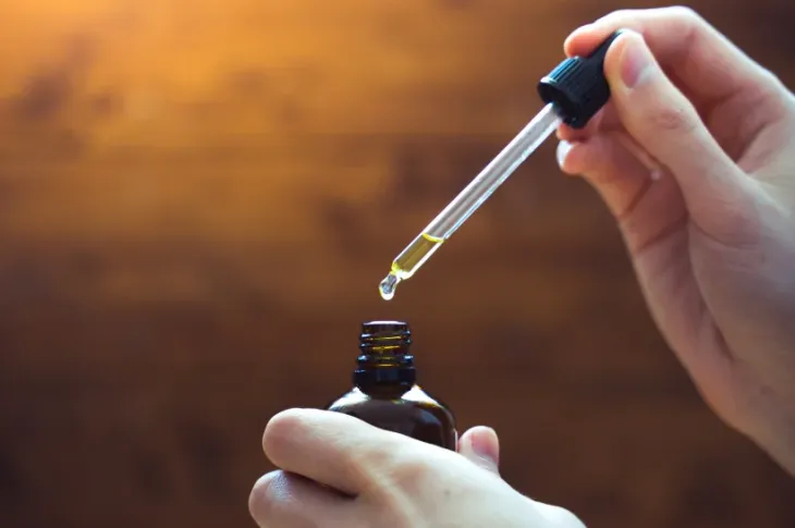 a hand holding a dropper over a small bottle of CBD oil