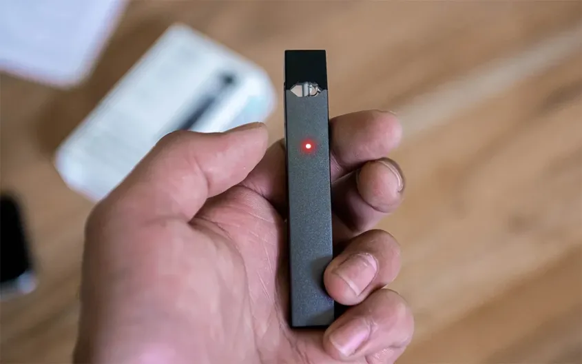 a hand holding a black vaping device with a red light